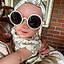 Layla is registered to the contest to win money with this photo: baby, child, sunglasses, headband, floral, portrait, person, holding, arm, hand, clothing, fashion, accessory, indoors, brick_wall, window, closeup, cute, face, smile