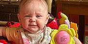 Layla joined the competition — help win amazing prizes! baby, child, walker, toy, red, floral_bib, indoor, wooden_chair, table, colorful, face, smiling, person, hands, playtime, cute, furniture, car_toy, expression, home