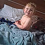Cash is registered to the contest to win money with this photo: bed, blanket, blue_blanket, child, cozy, curly_hair, cushion, happy, headboard, indoor, person, pillow, portrait, shirtless, smiling, soft_texture, stuffed_animal, toddler, toy, wood_panel