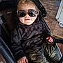 toddler, child, sunglasses, stroller, hoodie, curly_hair, smile, indoor, floor_tiles, camo_pants, hand, baby_clothing, seat, person, cute, casual, reflection, eyewear, cool, happy