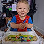 Cash is registered to the contest to win money with this photo: toddler, child, high_chair, spiderman_shirt, smiling, food, messy, indoor, tray, utensil, blond_hair, baby, happy, person, furniture, floor, room, plastic, table, cute