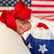 Becklynn is registered to the contest to win money with this photo: american_flag, baby, closeup, cushion, cute, face, flag, headwear, indoors, infant, nasal_tube, newborn, patriotic, peaceful, portrait, red_bow, resting, sleeping, soft, wrapped