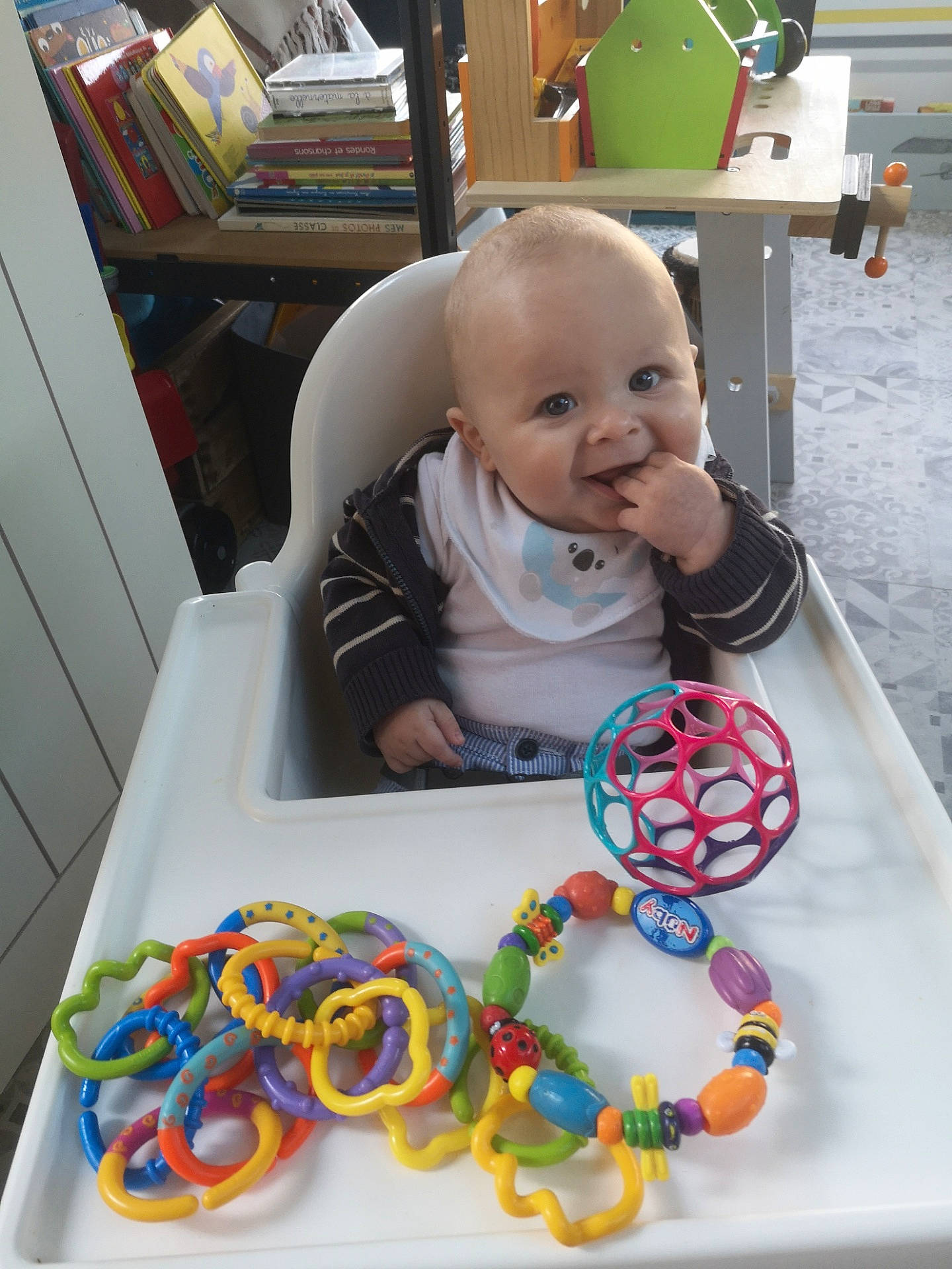 Eliot a rejoint le concours — aidez-le/la à gagner de superbes lots ! art, baby, baby_products, baby_toddler_clothing, bookcase, child, eye, fashion_accessory, flooring, fun, green, head, mouth, person, product, room, shelf, smile, toddler, toy