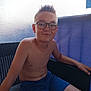 blue_shorts, boy, casual, child, confident, furniture, glasses, indoor, person, portrait, relaxing, shirtless, shorts, sitting, smile, spiky_hair, summer, texture, wicker_chair, young