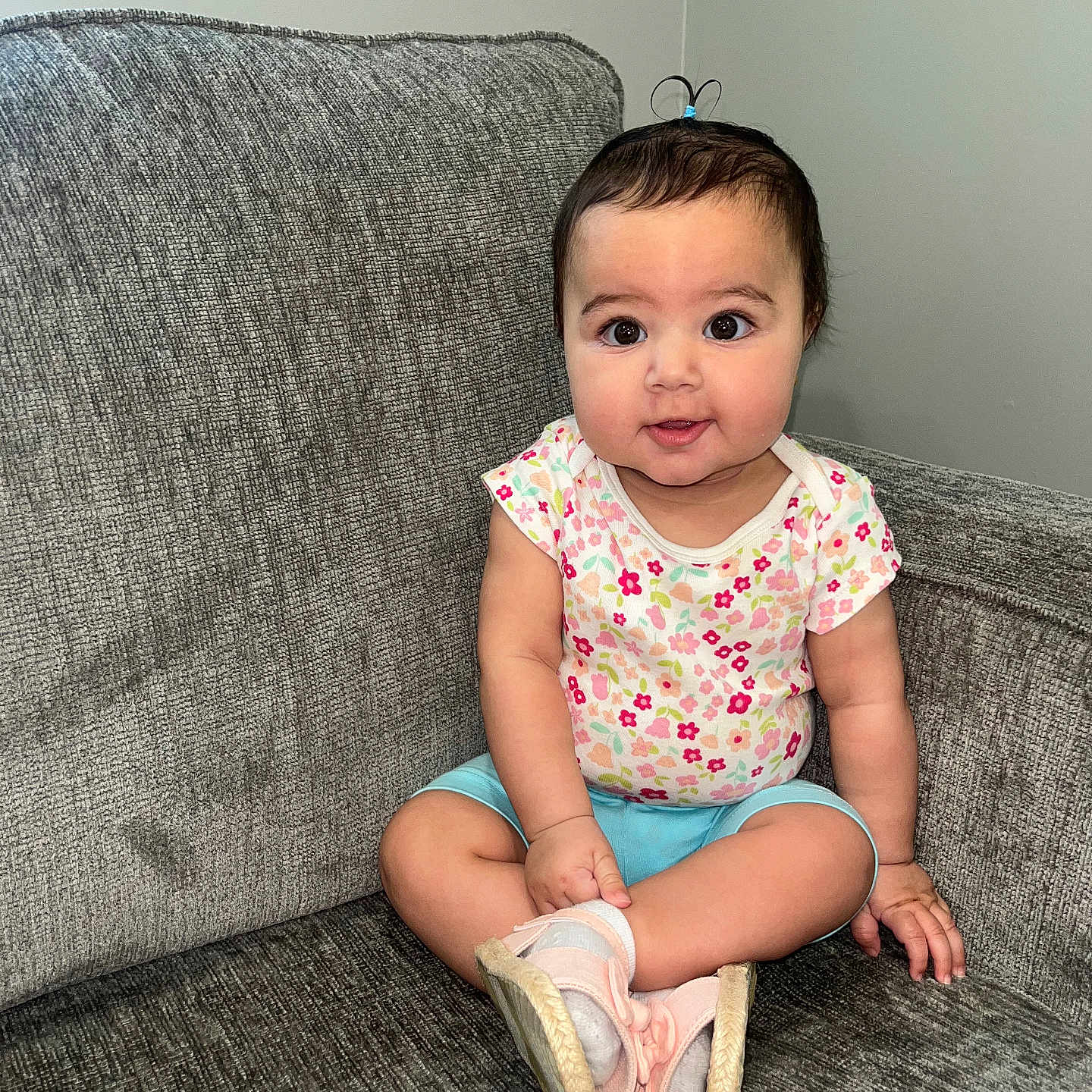 Lamees joined the competition — help win amazing prizes! baby, blue_shorts, child, couch, cross_legged, cute, face, floral_shirt, furniture, gray_couch, hair_tie, happy, indoors, person, pink_shoes, portrait, sitting, smiling, socks, young_child