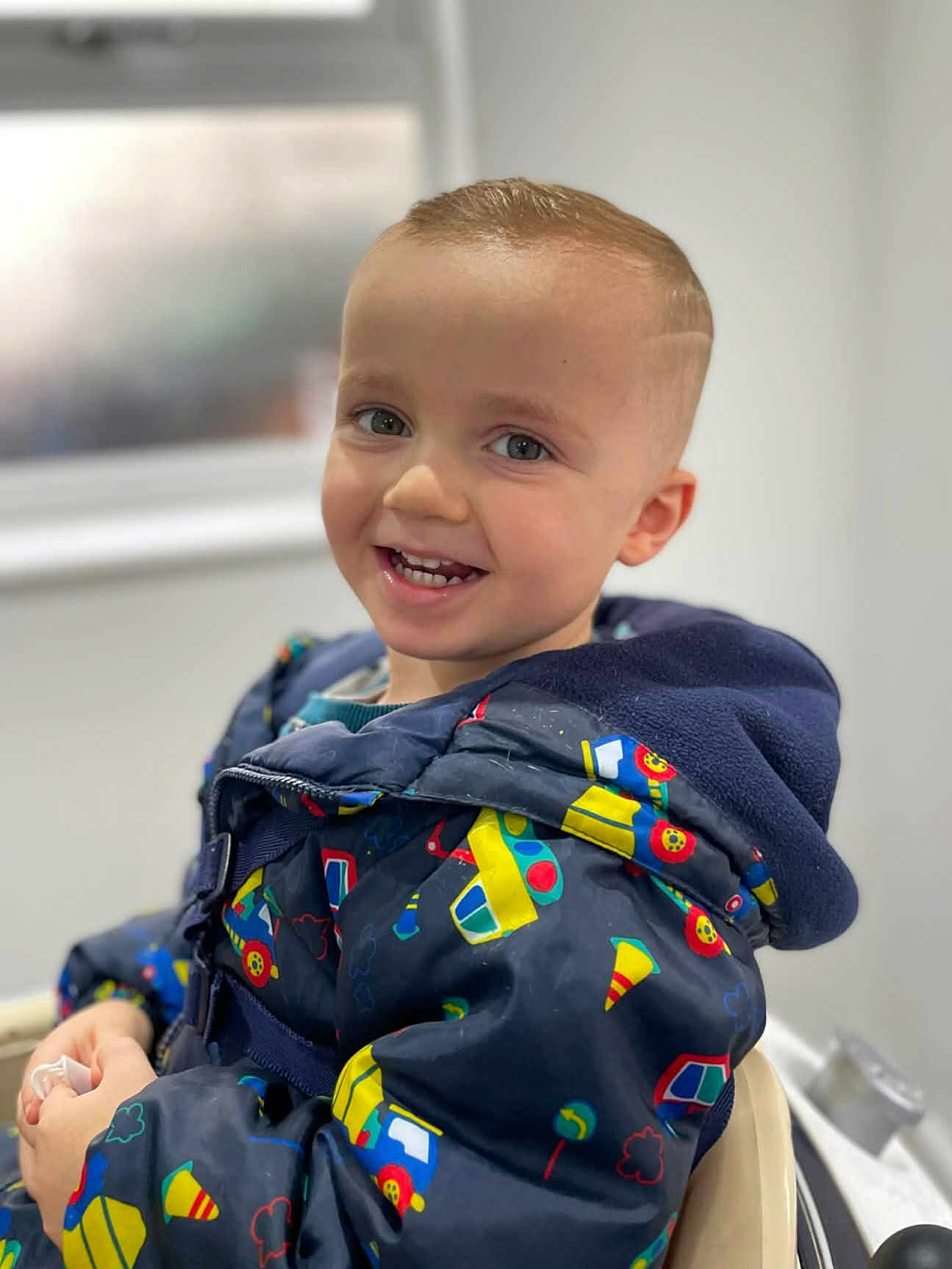 Brody joined the competition — help win amazing prizes! blurred_background, bright, casual, child, clothing, colorful, cute, face, happy, indoors, jacket, pattern, portrait, seat, short_hair, smiling, toddler, warm, window, young_child