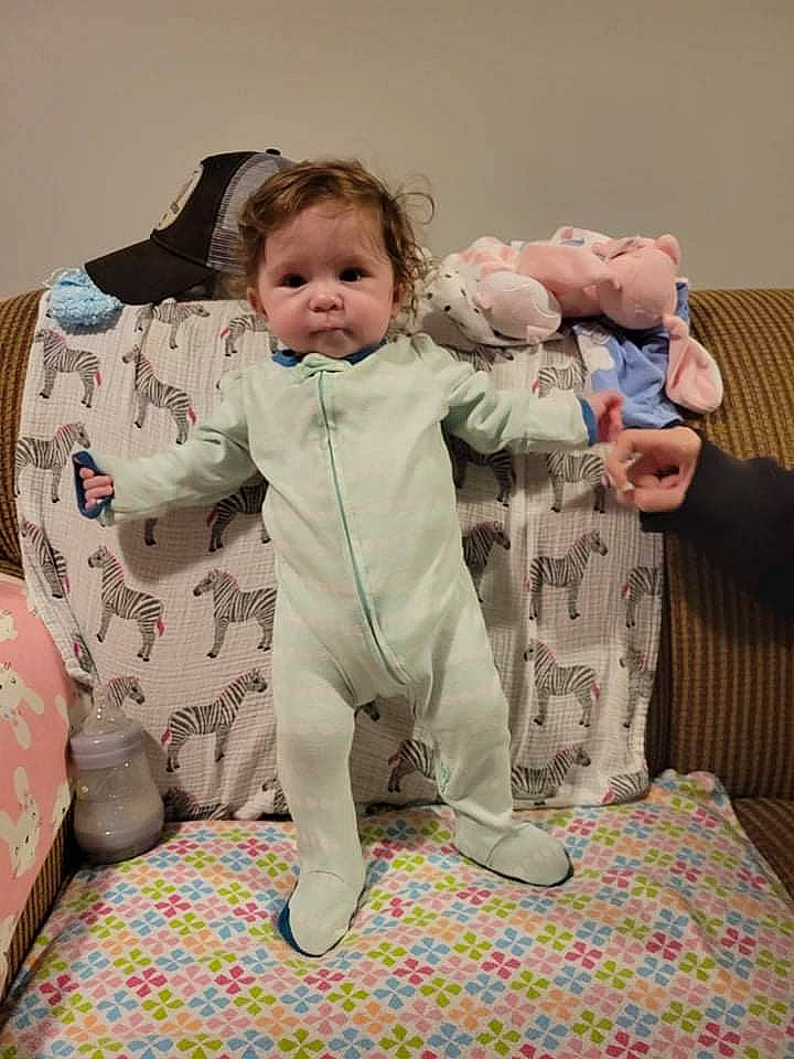 Rayna is registered to the contest to win money with this photo: baby, baby_toddler_clothing, child, comfort, facial_expression, fun, fur, gesture, hairstyle, happy, human, lap, linens, pajamas, person, room, sitting, sleeve, standing, textile