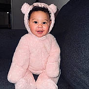 Kaleigha joined the competition — help win amazing prizes! baby, child, pink, bear_suit, costume, smiling, cute, fluffy, indoors, couch, seated, portrait, happy, curly_hair, face, cozy, soft, playful, infant, person