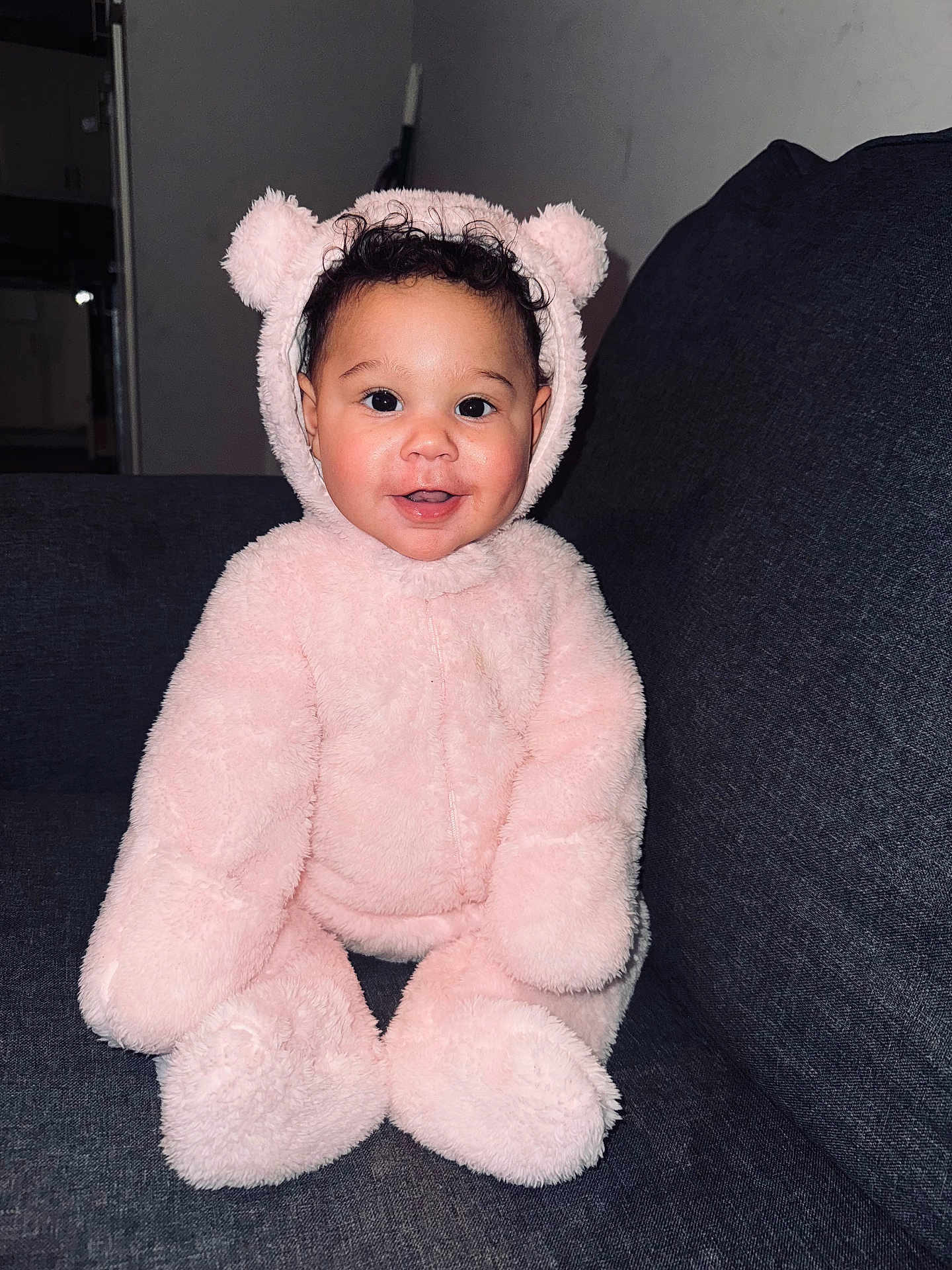 Kaleigha joined the competition — help win amazing prizes! baby, child, pink, bear_suit, costume, smiling, cute, fluffy, indoors, couch, seated, portrait, happy, curly_hair, face, cozy, soft, playful, infant, person