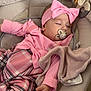 baby, infant, sleeping, pacifier, headband, bow, pink_clothing, plaid_pants, blanket, bassinet, bedding, plush_toy, hand, closed_eyes, newborn, cozy, soft_fabric, nursery, portrait, peaceful