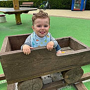 Kailan a rejoint le concours — aidez-le/la à gagner de superbes lots ! toddler, child, toy_car, wooden_toy, playground, green_surface, bench, bicycle, book_kiosk, outdoor, smiling, tongue_out, bib, casual_clothing, curly_hair, daylight, play, fun, wood, nature