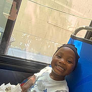 Aijalon is registered to the contest to win money with this photo: child, smiling, boy, seat, window, reflection, cap, shirt, starfish, indoor, daylight, plastic_bag, happy, portrait, casual, candid, sidewalk, wall, blue_seat, person