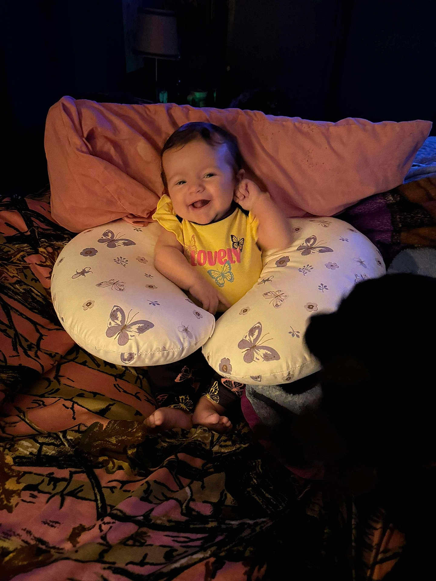 Raelynn joined the competition — help win amazing prizes! baby, smiling, yellow_shirt, nursing_pillow, butterfly_pattern, bedspread, pink_pillow, cozy, dim_lighting, happy, infant, child, indoor, dog_silhouette, feet, cute, person, portrait, furniture, relaxed