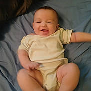 Paige joined the competition — help win amazing prizes! baby, infant, smiling, lying_down, onesie, bed, blue_bedspread, happy, chubby_legs, arms, face, skin, head, cute, child, person, indoor, soft_lighting, motion_blur, playful