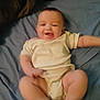 baby, infant, smiling, lying_down, onesie, bed, blue_bedspread, happy, chubby_legs, arms, face, skin, head, cute, child, person, indoor, soft_lighting, motion_blur, playful