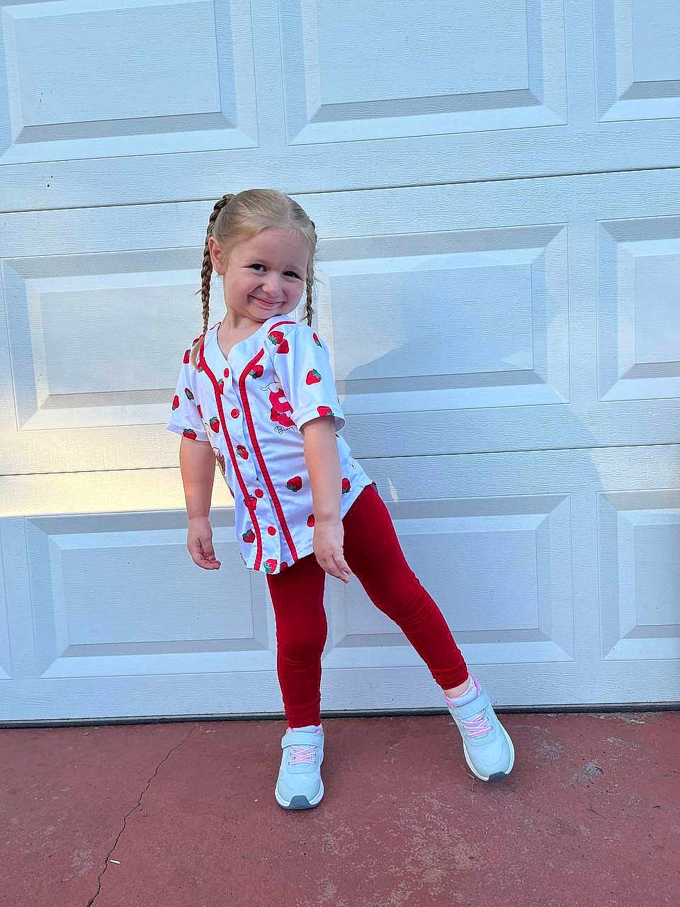 Emily joined the competition — help win amazing prizes! child, girl, braided_hair, smile, playful_pose, white_shirt, strawberry_pattern, red_leggings, sneakers, outdoor, garage_door, concrete, shadow, sunlight, casual_clothing, happy, person, portrait, standing, cute
