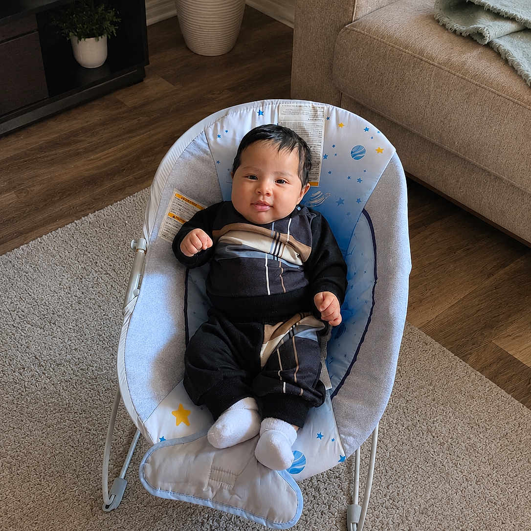 Yetziel joined the competition — help win amazing prizes! baby, infant, baby_rocker, clothing, white_socks, face, person, carpet, living_room, couch, plant, potted_plant, wood_floor, furniture, indoor, smiling, comfort, cute, home_decor, relaxation