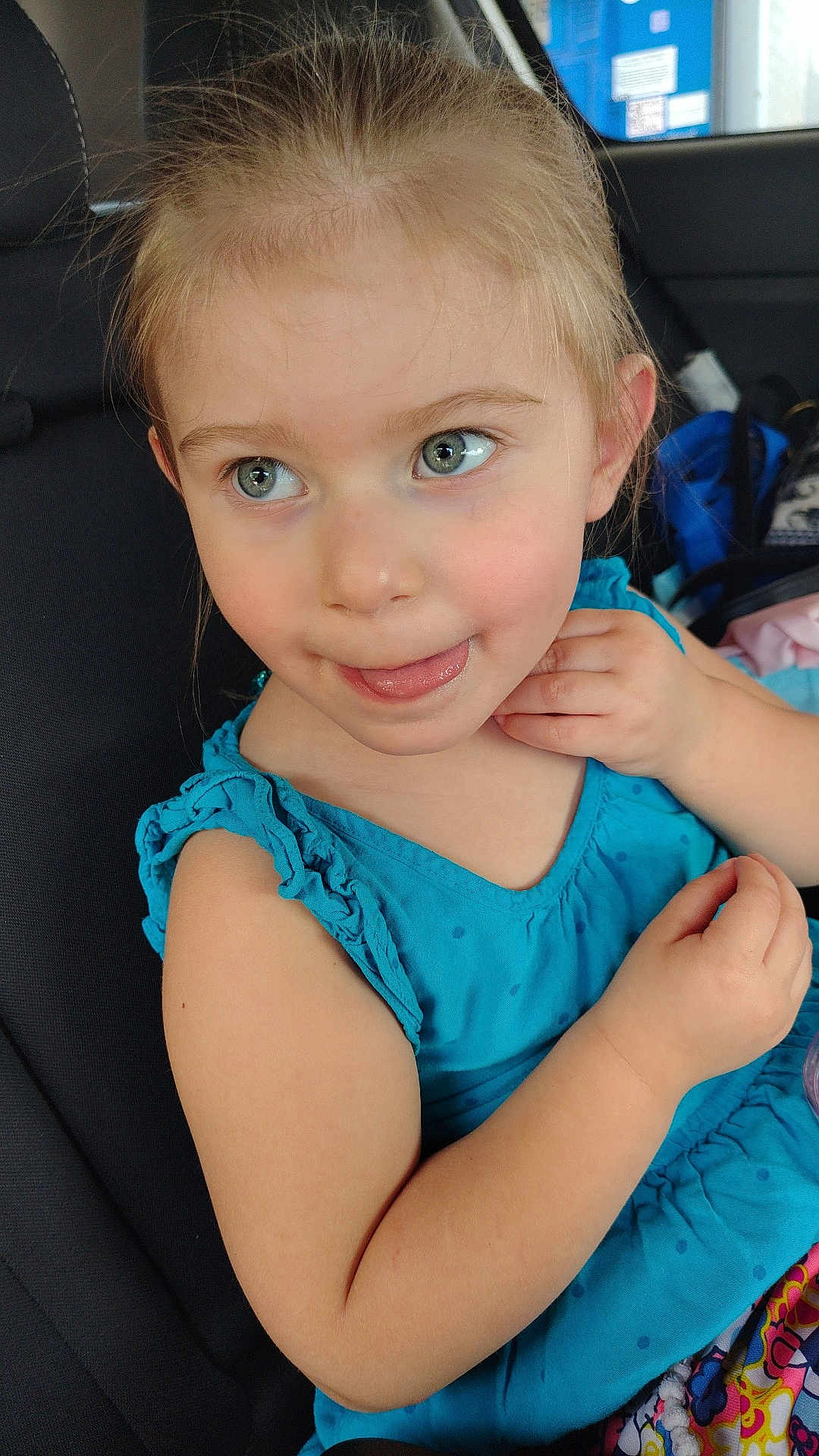 Athena is registered to the contest to win money with this photo: child, girl, blue_eyes, car_seat, turquoise_dress, smile, tongue_out, hand, seatbelt, vehicle_interior, playful, cute, young_child, casual_clothing, portrait, human, person, seat, indoor, closeup