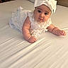 baby, infant, white_dress, headband, bow, bed, bedding, cute, chubby_cheeks, portrait, child, indoor, soft_lighting, curious, lying_down, person, young_child, adorable, sleepwear, cozy