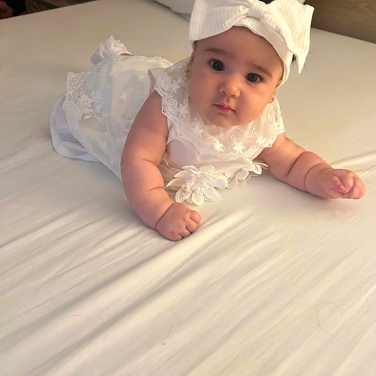 Kathleen joined the competition — help win amazing prizes! baby, infant, white_dress, headband, bow, bed, bedding, cute, chubby_cheeks, portrait, child, indoor, soft_lighting, curious, lying_down, person, young_child, adorable, sleepwear, cozy