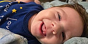 Leo is registered to the contest to win money with this photo: baby, smiling, tongue, blanket, blue_shirt, stars, face, closeup, happy, infant, soft_texture, child, cute, indoors, person, portrait, skin, head, expression, resting