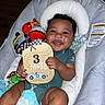 Fidel is registered to the contest to win money with this photo: baby, smile, infant, child, toy, blanket, cushion, seat, wooden_sign, clothing, happy, face, hand, indoor, diaper, photography, cute, play, holding, portrait