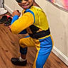 child, superhero_costume, sunglasses, pose, smile, indoor, wooden_floor, wall, tapestry, colorful, reflection, footwear, socks, hair, braids, playful, bright_colors, person, young, fun