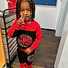 child, boy, smiling, hand_gesture, spiderman_outfit, red_clothing, black_clothing, braided_hair, indoor, flooring, door, drawer, blue_board, casual, portrait, person, playful, young_child, boots, peace_sign