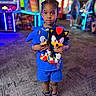 child, arcade, plush_toys, sonic, shadow, blue_clothing, indoor, carpet, neon_lights, gaming, person, shoes, toy, standing, young, face, holding, colorful, blurred_background, entertainment