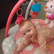 Paisley is registered to the contest to win money with this photo: baby, blue_eyes, carpet, child, cute, face, happy, indoor, infant, lying_down, orange, person, pink, play_mat, smiling, soft_toys, striped_clothing, stuffed_animal, toy, white