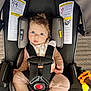 baby, car_seat, child, infant, straps, warning_labels, toy, pink_clothing, blue_eyes, hair, seatbelt, safety, indoors, car_seat_cushion, red_button, curious_expression, skin, foot, hand, closeup