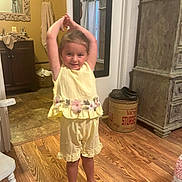 Ella joined the competition — help win amazing prizes! child, girl, toddler, smiling, standing, stretching, arms_up, yellow_outfit, dress, floral_pattern, barefoot, indoors, bathroom, mirror, sink, towel, wooden_floor, furniture, storage_barrel, portrait