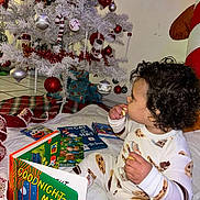 Mateo joined the competition — help win amazing prizes! toddler, child, christmas_tree, pajamas, books, snack, holiday, curly_hair, indoor, decorations, white_tree, ornaments, blanket, reading, festive, cozy, floor, present, toy, cute