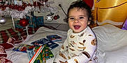 Mateo is registered to the contest to win money with this photo: toddler, child, smiling, pajamas, cookie_pattern, book, reading, christmas_tree, ornaments, white_tree, holiday, indoor, blanket, floor, decorations, happy, festive, toy, present, cozy