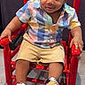 toddler, child, rocking_chair, red_chair, colorful_shirt, shorts, sneakers, floor, indoor, smile, happy, cute, portrait, seated, wooden_chair, footwear, person, young_child, fashion, casual_clothing