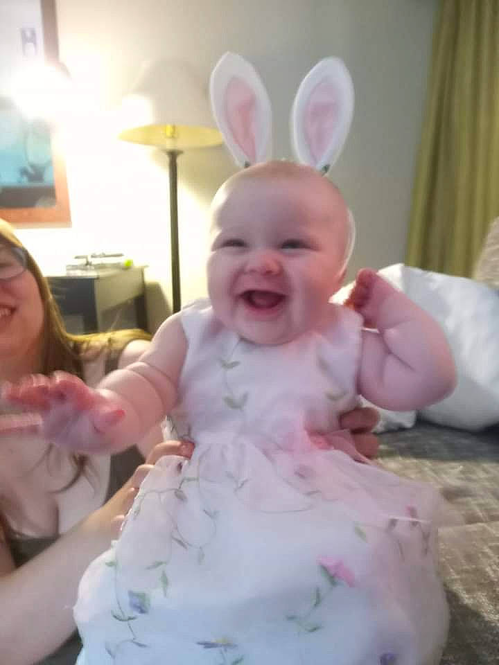 Cora is registered to the contest to win money with this photo: baby, child, curtain, ear, event, finger, fun, gesture, happy, hat, joy, lamp, lighting, party_supply, person, pink, room, sitting, skin, smile