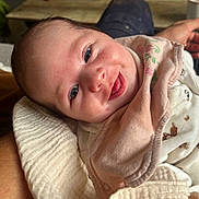 Gabriella a rejoint le concours — aidez-le/la à gagner de superbes lots ! baby, smiling, face, blanket, bib, clothing, person, infant, hand, happy, closeup, indoor, table, wood, fabric, skin, cute, portrait, newborn, cozy