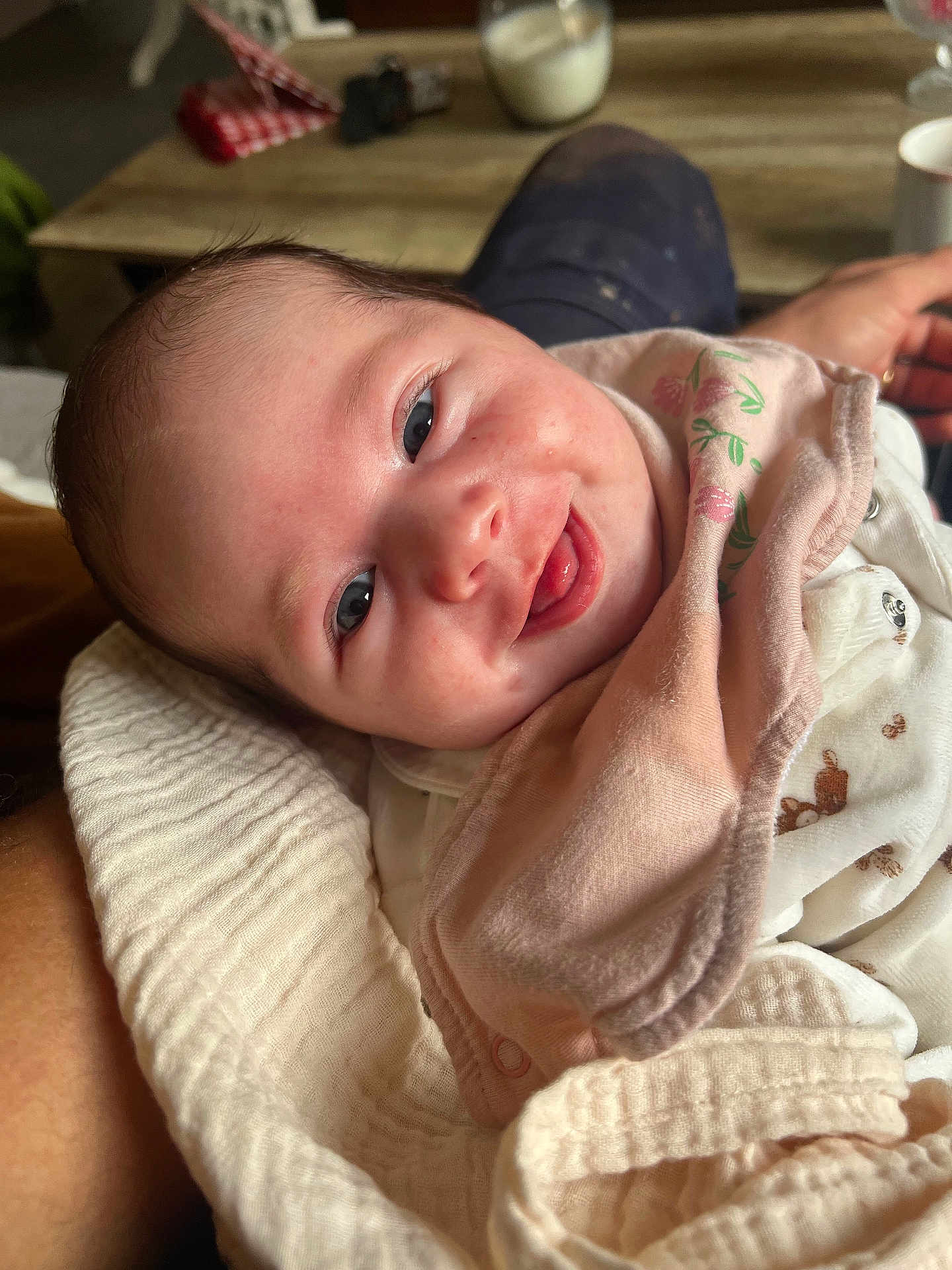 Gabriella a rejoint le concours — aidez-le/la à gagner de superbes lots ! baby, smiling, face, blanket, bib, clothing, person, infant, hand, happy, closeup, indoor, table, wood, fabric, skin, cute, portrait, newborn, cozy