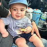 Gabriel joined the competition — help win amazing prizes! baby, child, infant, cap, blue_cap, gray_shirt, shorts, food, bread, car_interior, seat, adult_hand, water_bottle, travel_mug, happy, cute, portrait, person, sitting, closeup