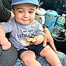 baby, child, cap, cookie, denim_shorts, person, car_interior, water_bottle, seat, hand, smile, toddler, clothing, sitting, lap, cute, face, casual, food, parent