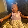 Lyndon is registered to the contest to win money with this photo: baby, child, girl, sitting, chair, blanket, clothing, purple_top, floral_pants, bows, jewelry, necklace, bracelet, smiling, indoors, cozy, comfort, cute, person, portrait