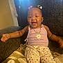 Lyndon is registered to the contest to win money with this photo: baby, child, smiling, sitting, indoor, blanket, chair, purple_top, floral_pants, gold_chain, hair_bows, happy, cute, cozy, infant, portrait, furniture, soft_light, person, toddler