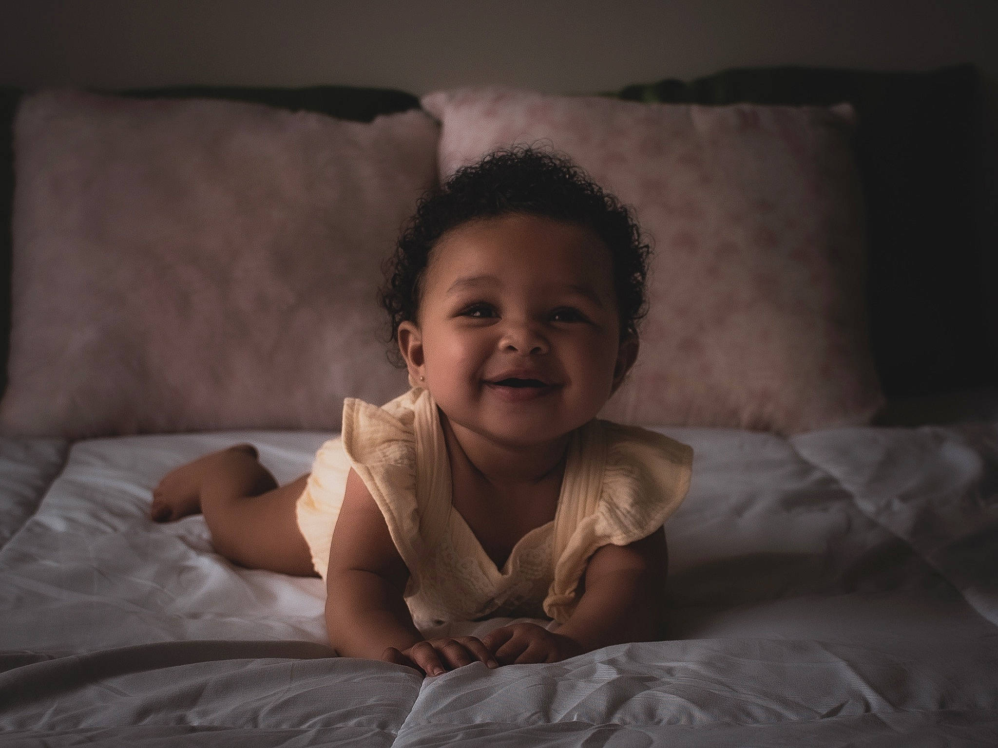 Astoria is registered to the contest to win money with this photo: baby, bedding, child, comfort, darkness, flash_photography, flooring, fun, happy, joy, linens, monochrome, monochrome_photography, person, pillow, portrait_photography, room, sitting, smile, throw_pillow