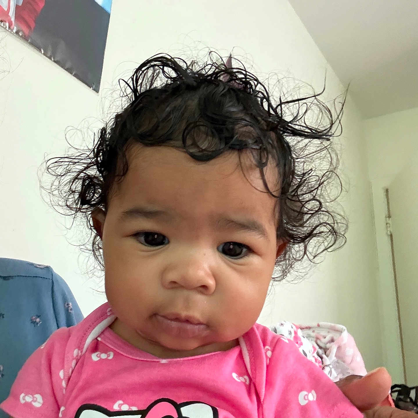 Kaoir is registered to the contest to win money with this photo: baby, child, clothing, curly_hair, cute, door, expression, face, furniture, hand, hello_kitty, holding, home, indoor, person, pink_clothing, portrait, toddler, wall, young_child