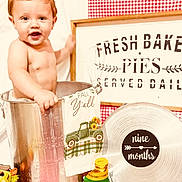 Kallen joined the competition — help win amazing prizes! baby, child, metal_bucket, kitchen, decor, sign, towel, pie_tin, nine_months, gingham, red_background, vintage_truck, sunflowers, smiling, portrait, indoor, milestone, cute, playful, props