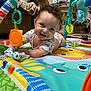 Orion is registered to the contest to win money with this photo: baby, smiling, play_mat, toy, indoor, child, colorful, curly_hair, happy, crawling, fabric, living_room, pillow, blanket, person, furniture, floor, cute, infant, playtime