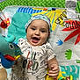 baby, smiling, dinosaur_onesie, hat, play_mat, toy, plush_toy, colorful, infant, happy, child, lying_down, cute, patterned_clothing, cheerful, indoors, playtime, bright_colors, closeup, hand