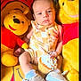 baby, child, cupcake, toy, stuffed_animal, winnie_the_pooh, plush, yellow, red, socks, shoes, face, expression, sitting, indoor, background, patterned_clothing, food, sprinkles, cute