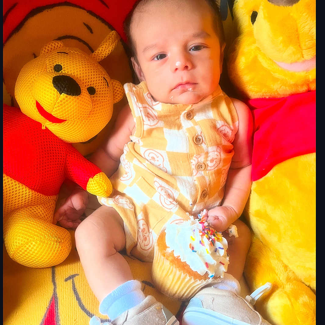 Luka joined the competition — help win amazing prizes! baby, background, child, cupcake, cute, expression, face, food, indoor, patterned_clothing, plush, red, shoes, sitting, socks, sprinkles, stuffed_animal, toy, winnie_the_pooh, yellow