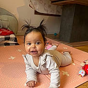 Tia participe au concours pour gagner de l'argent avec cette photo : baby, child, clothing, cute, face, floor, hair_pigtails, happy, home, indoor, infant, lying_down, person, pink_mat, playful, portrait, smiling, toy, wooden_floor, young_child
